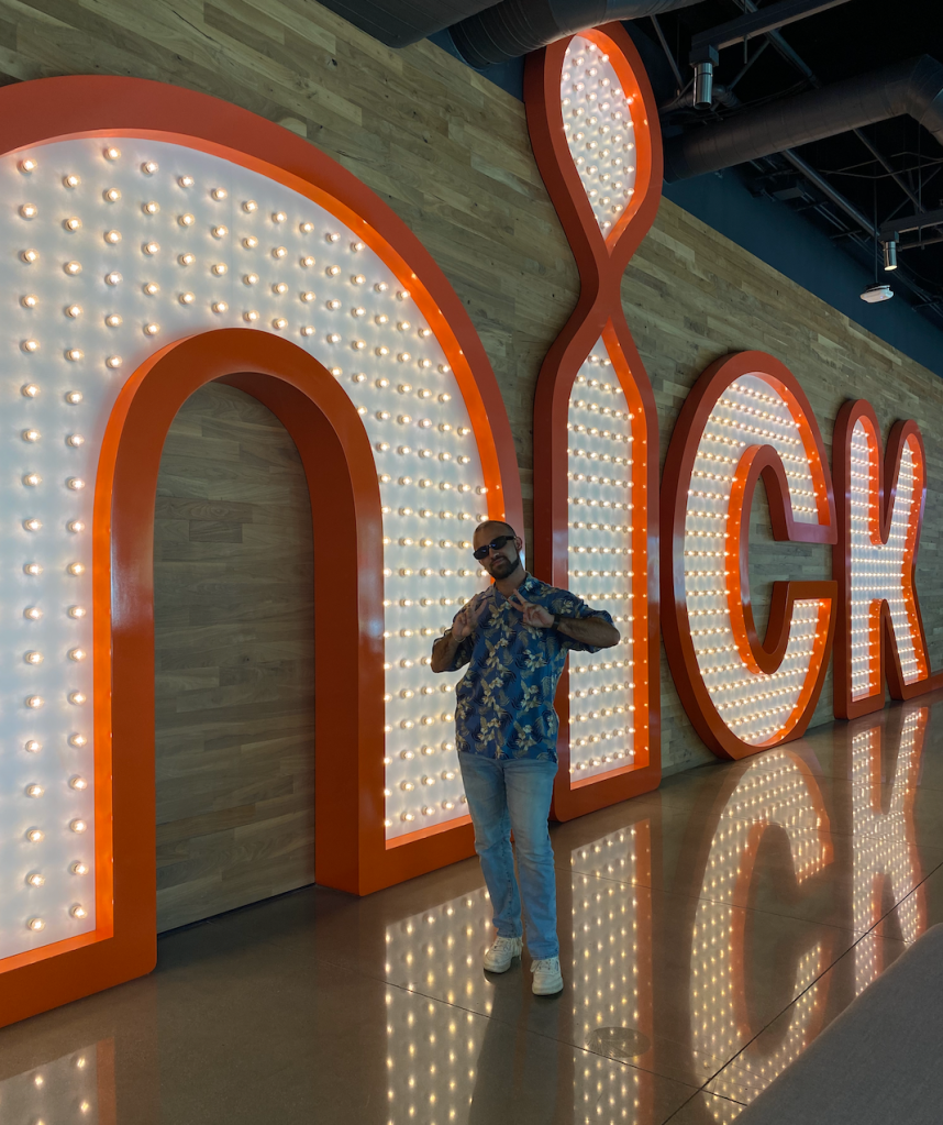 Picture of Emanuel in front of the light up Nick sign at work